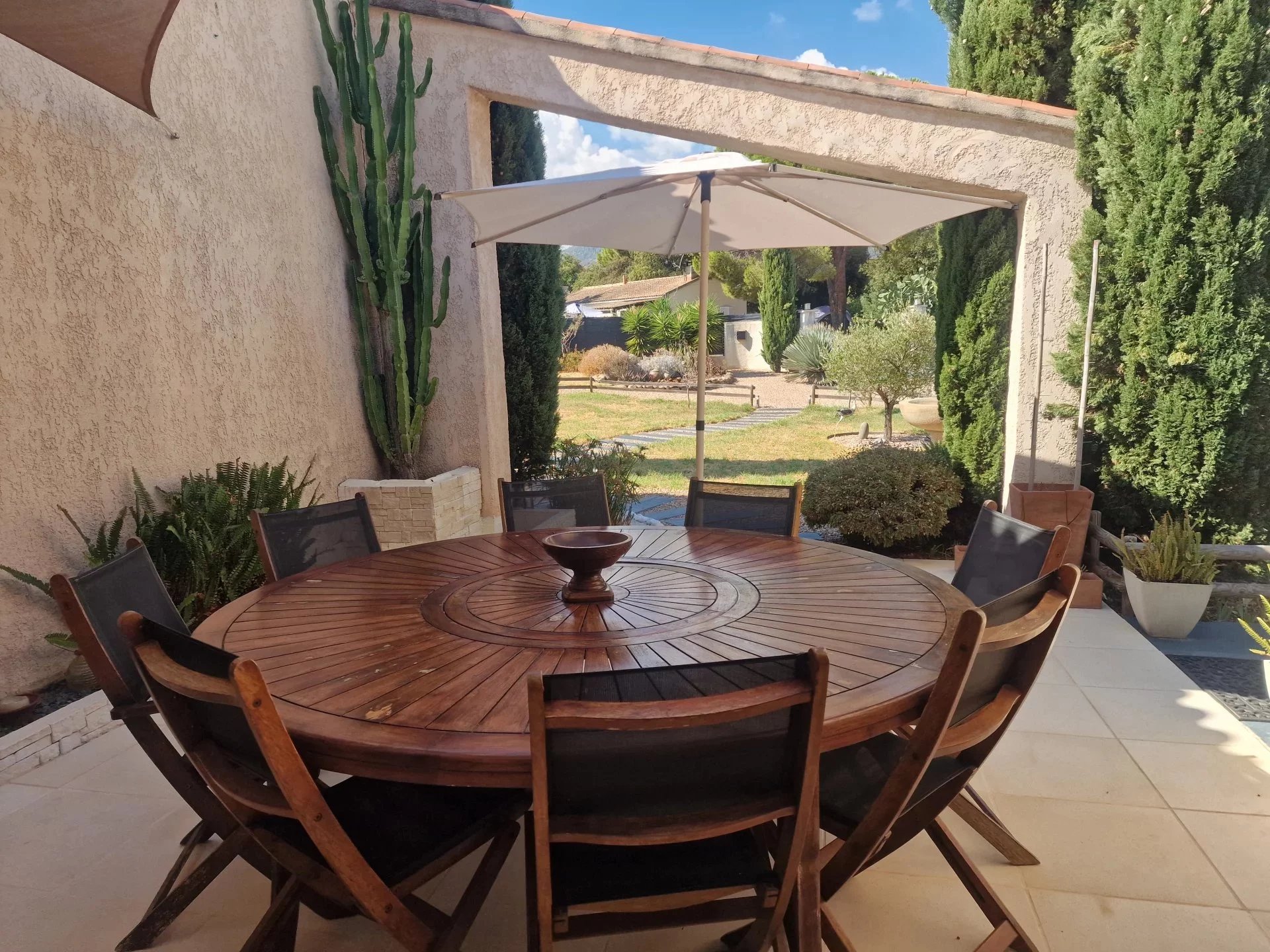 Terrasse de la villa à Marine de Solaro Terrasse avec table ronde en bois et chaises, entourée de végétation dans une villa en Corse.