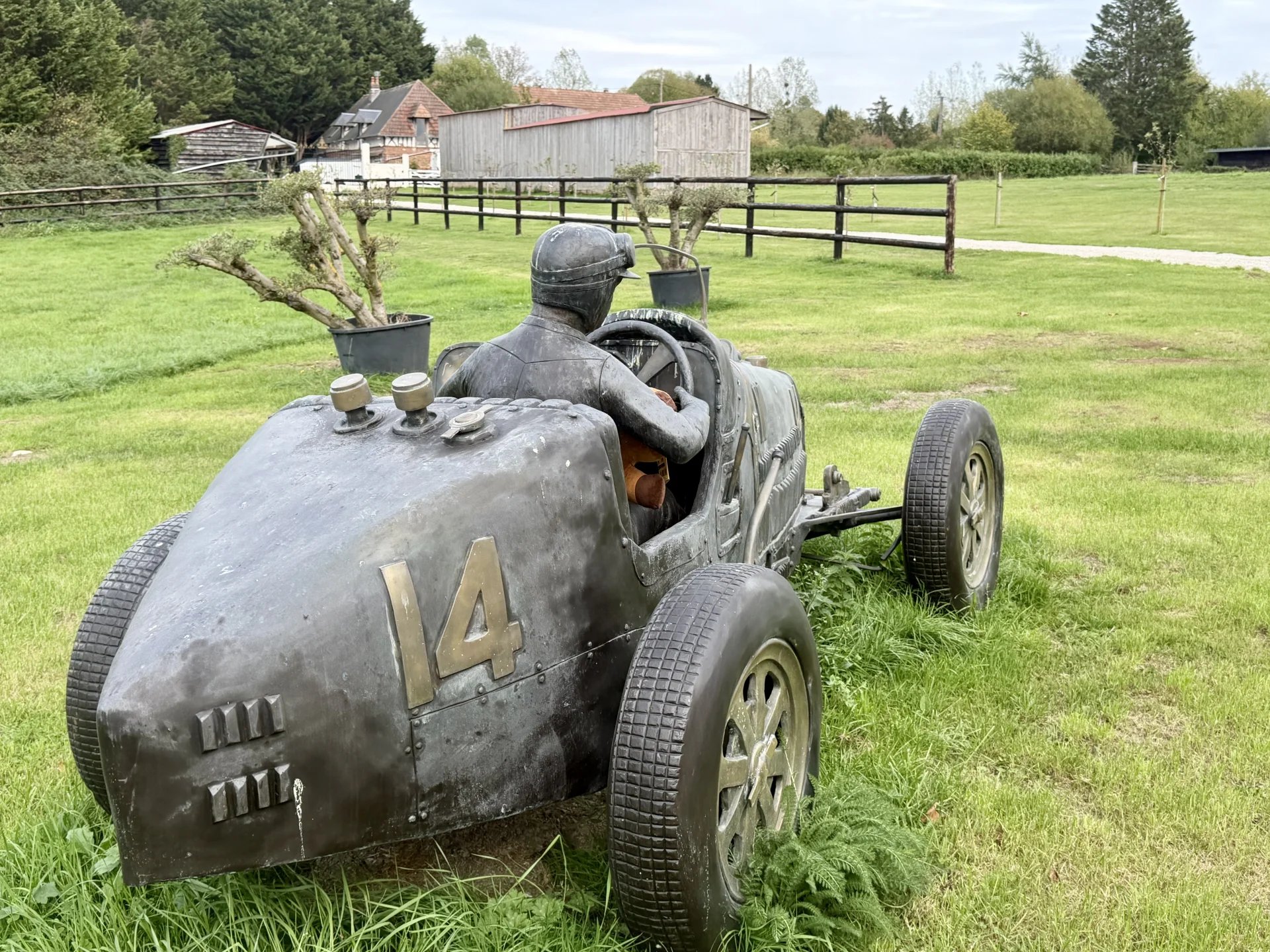 Statue de pilote de course Statue d'un pilote de course en métal sur une voiture ancienne dans un champ.