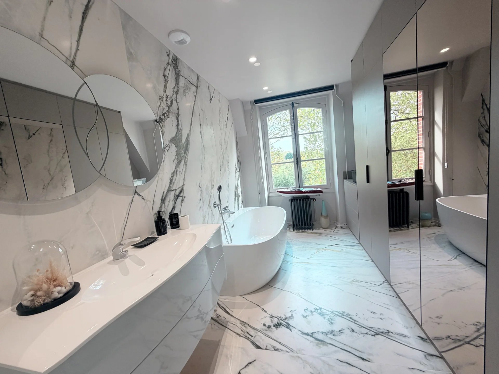 Salle de bain du château près de Pont-l’Évêque Salle de bain moderne avec baignoire et fenêtre donnant sur le jardin.