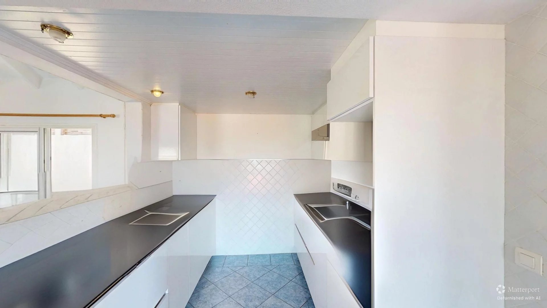 Bright white galley kitchen with dark countertops, white cabinets, and a double sink on the right.