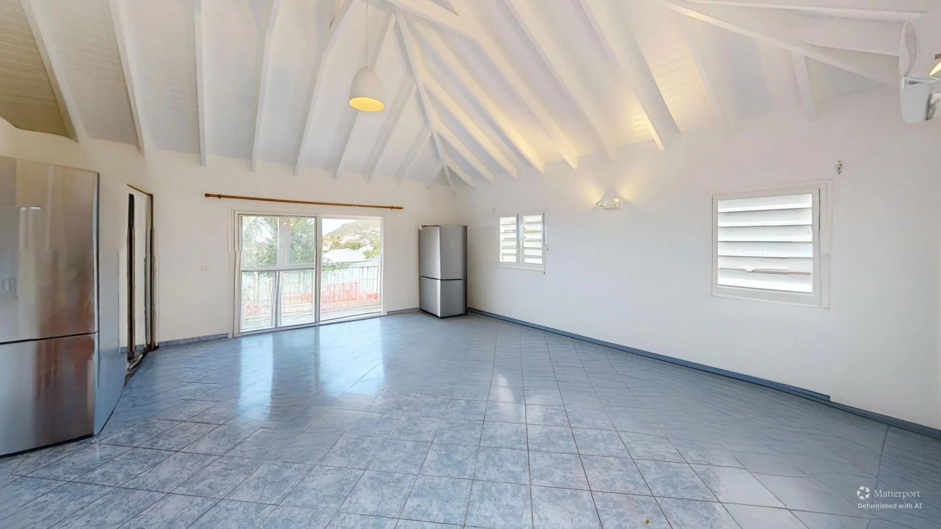 Bright, empty modern kitchen/lamily room with vaulted white beams, blue tile floor, and stainless steel fridge near a sliding glass door to a balcony.