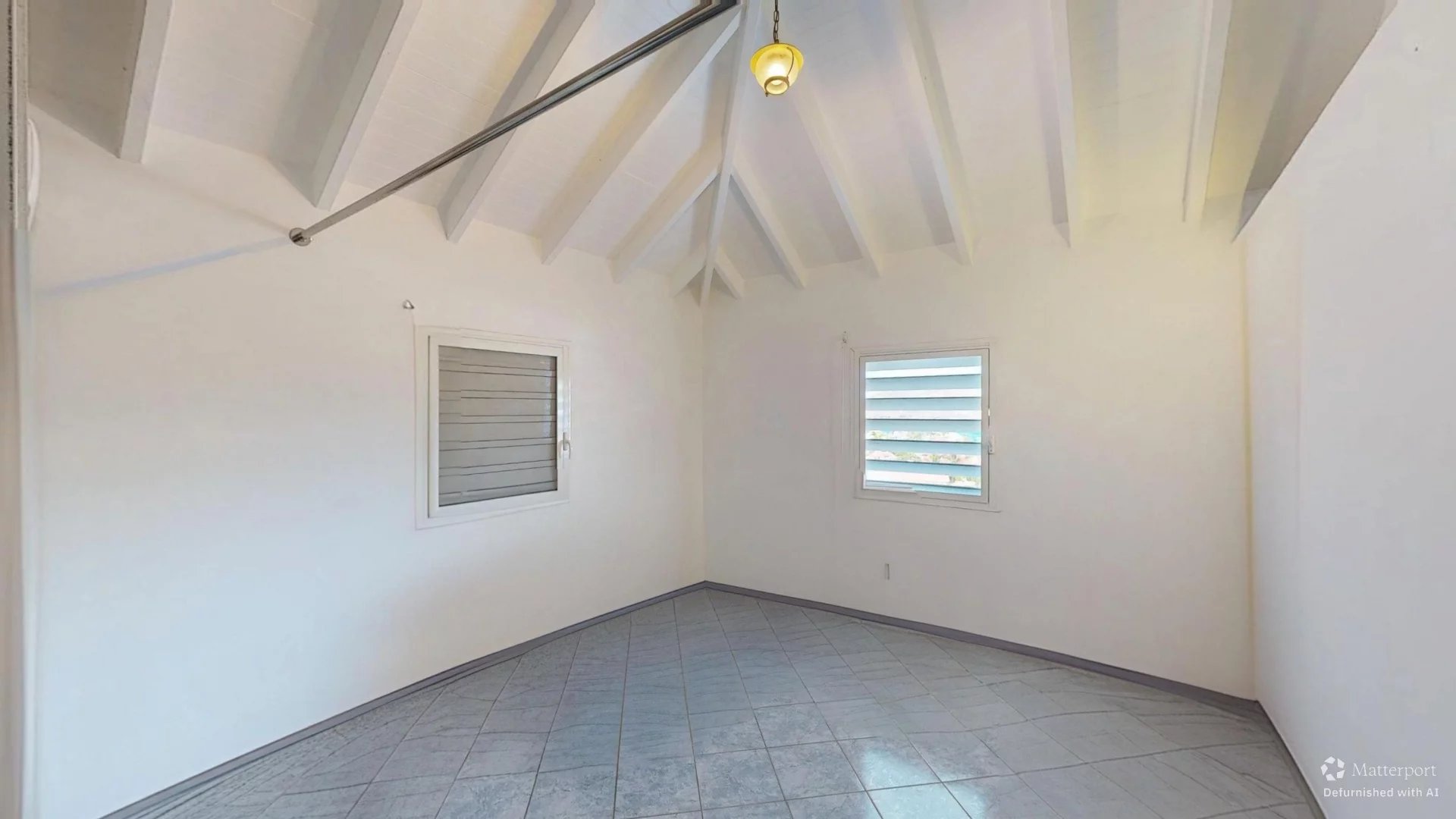 White room with vaulted ceiling and exposed beams, two small windows, and tiled floor.