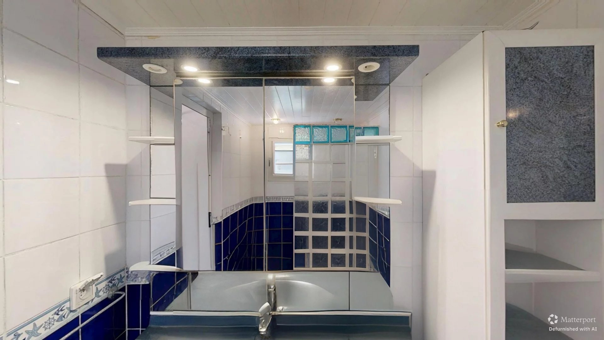 Bright bathroom with white walls, blue tile wainscoting, a glass shower enclosure, and white storage cabinets.