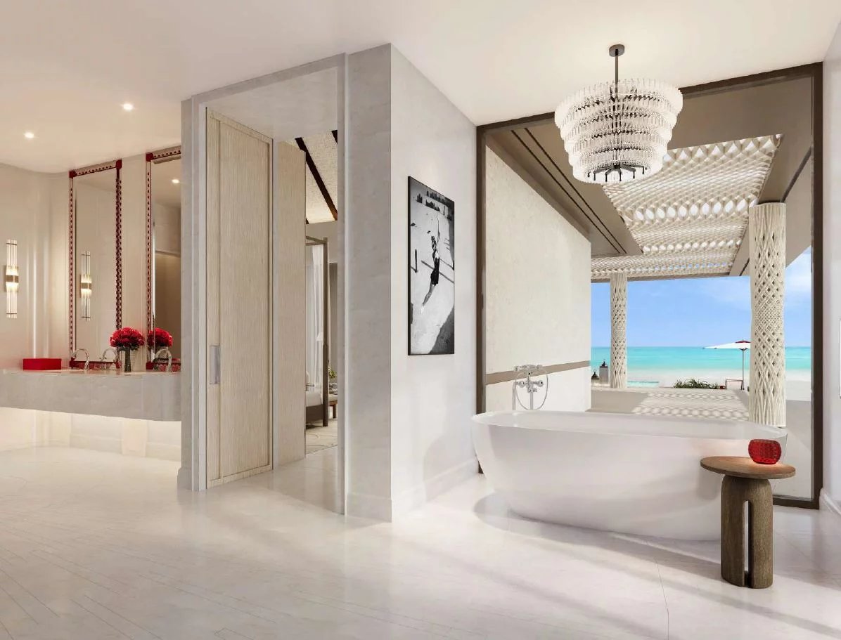 Luxurious white bathroom with a freestanding tub facing an ocean view, crystal chandelier, and light wood accents.