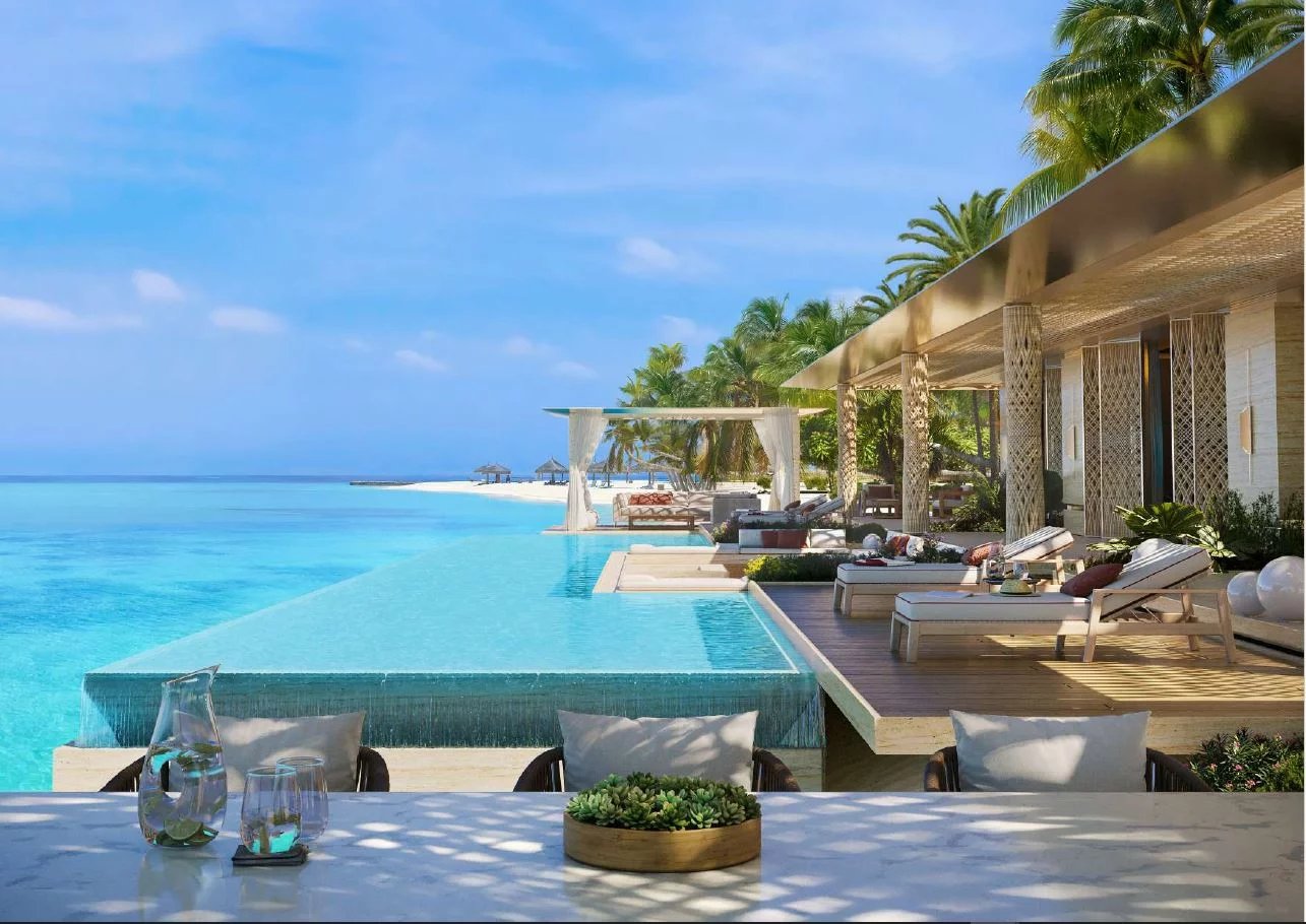 Infinity pool along a wooden deck at a tropical resort, with lounge chairs and palm trees overlooking the sea.