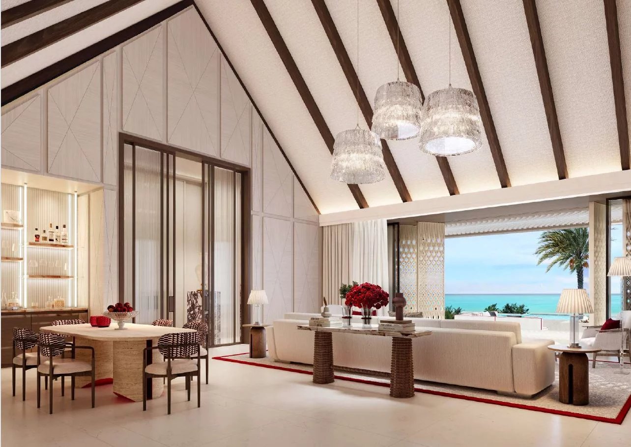 Luxurious open-plan living and dining area with a vaulted ceiling and dark wood beams, overlooking the beach and ocean through glass doors.