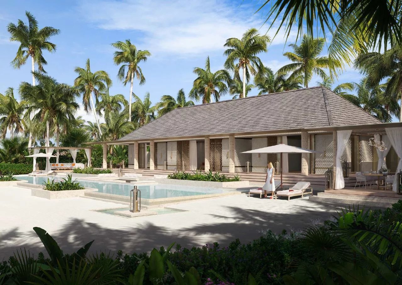 Luxury resort with a thatched villa, palm trees, and a poolside area; a woman in a white dress stands by lounge chairs under a parasol