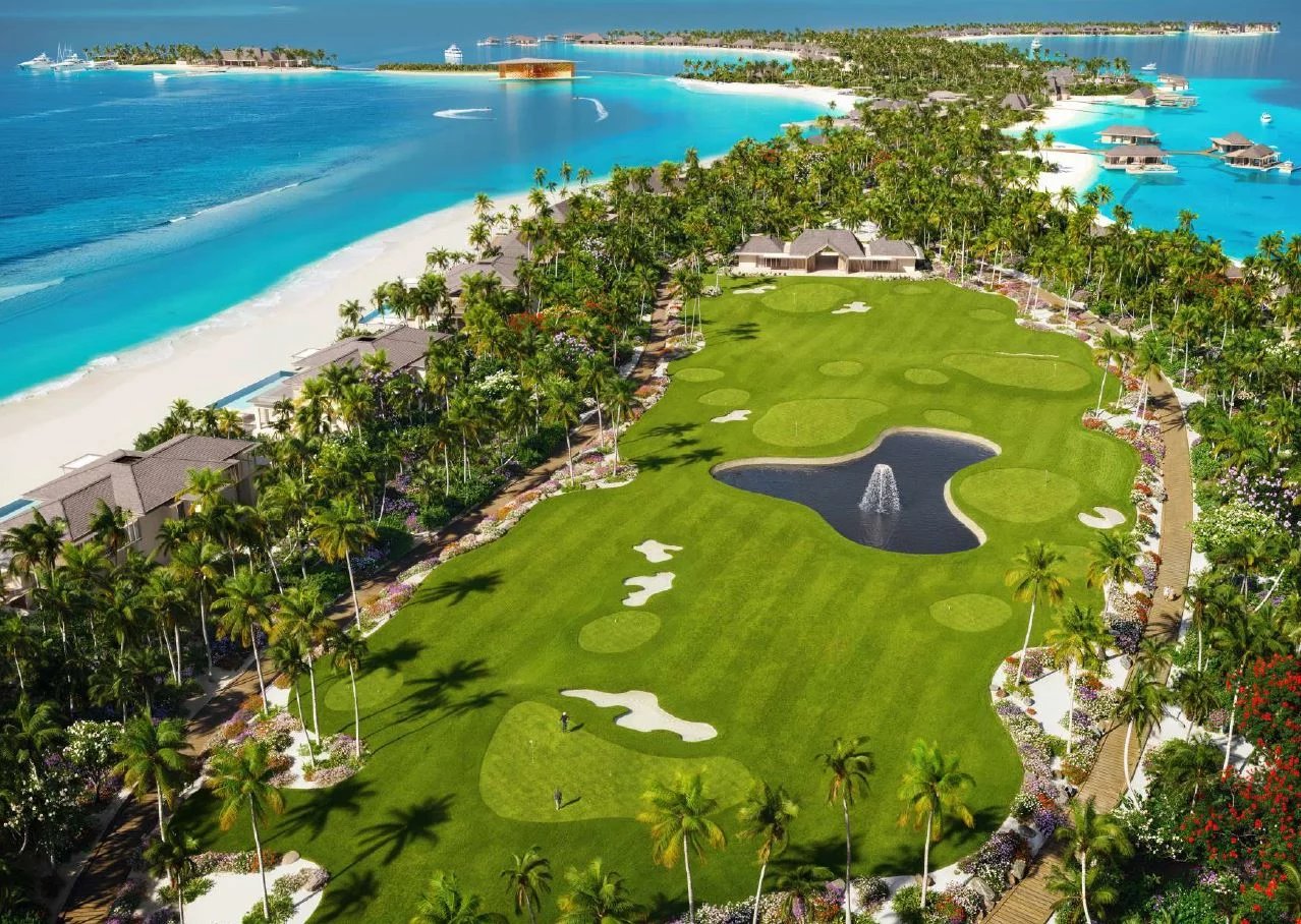Aerial view of a tropical resort golf course along a white-sand beach with palm trees and turquoise water surrounding green fairways.