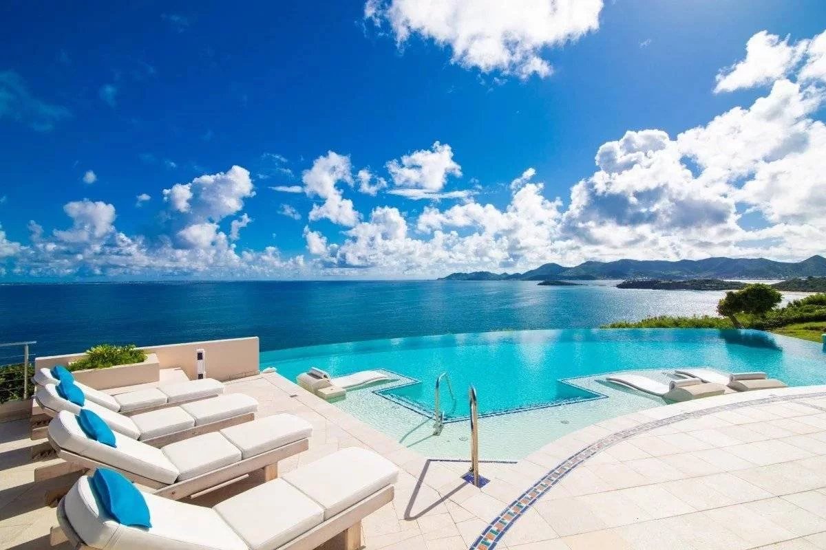 Infinity pool with white loungers and blue towels, overlooking a blue ocean and distant mountains.