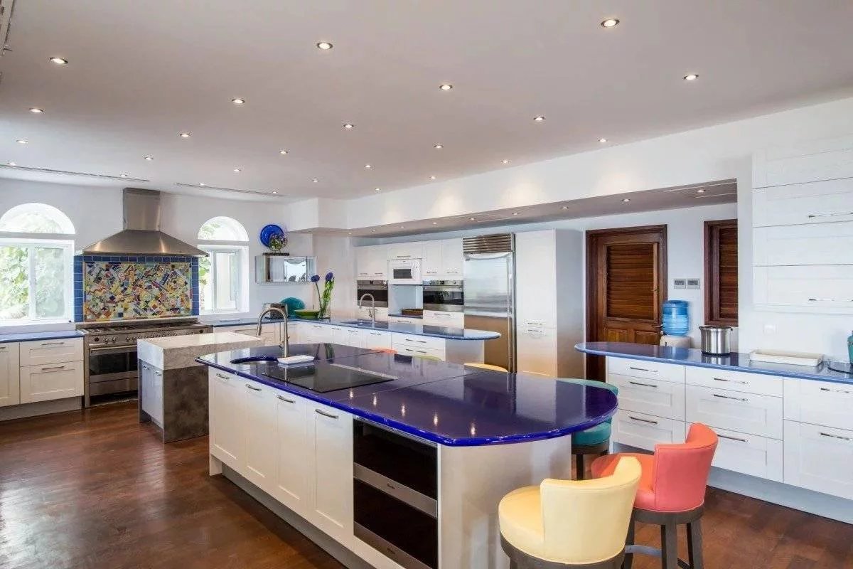Bright modern kitchen with a large central island, blue counters, and white cabinetry; mosaic tile backsplash near stainless steel range.