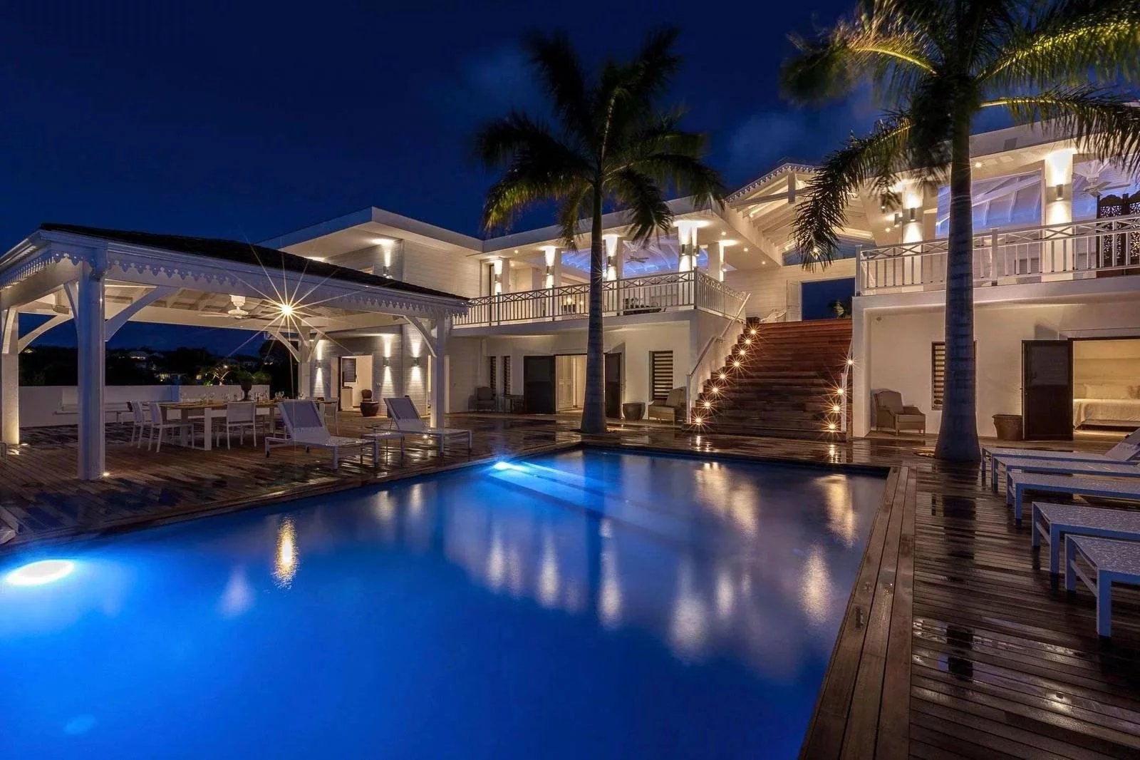 716f736d3df25a8b9215a942342f2495_edde2c976d_1600-original Luxurious nighttime pool terrace of a white tropical villa with palm trees and glowing deck lights.