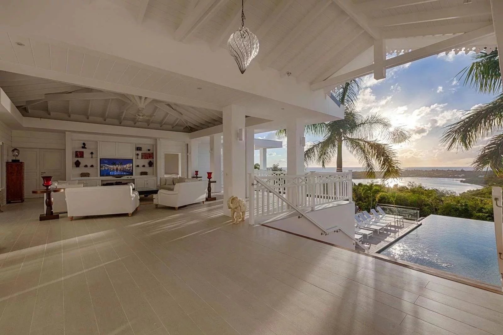 95ebaf42495da92d34de848b56193219_f87b0e66c1_1600-original Open-plan living area with white sofas, built-in shelves, and a TV, opening to a bright outdoor space and ocean view.