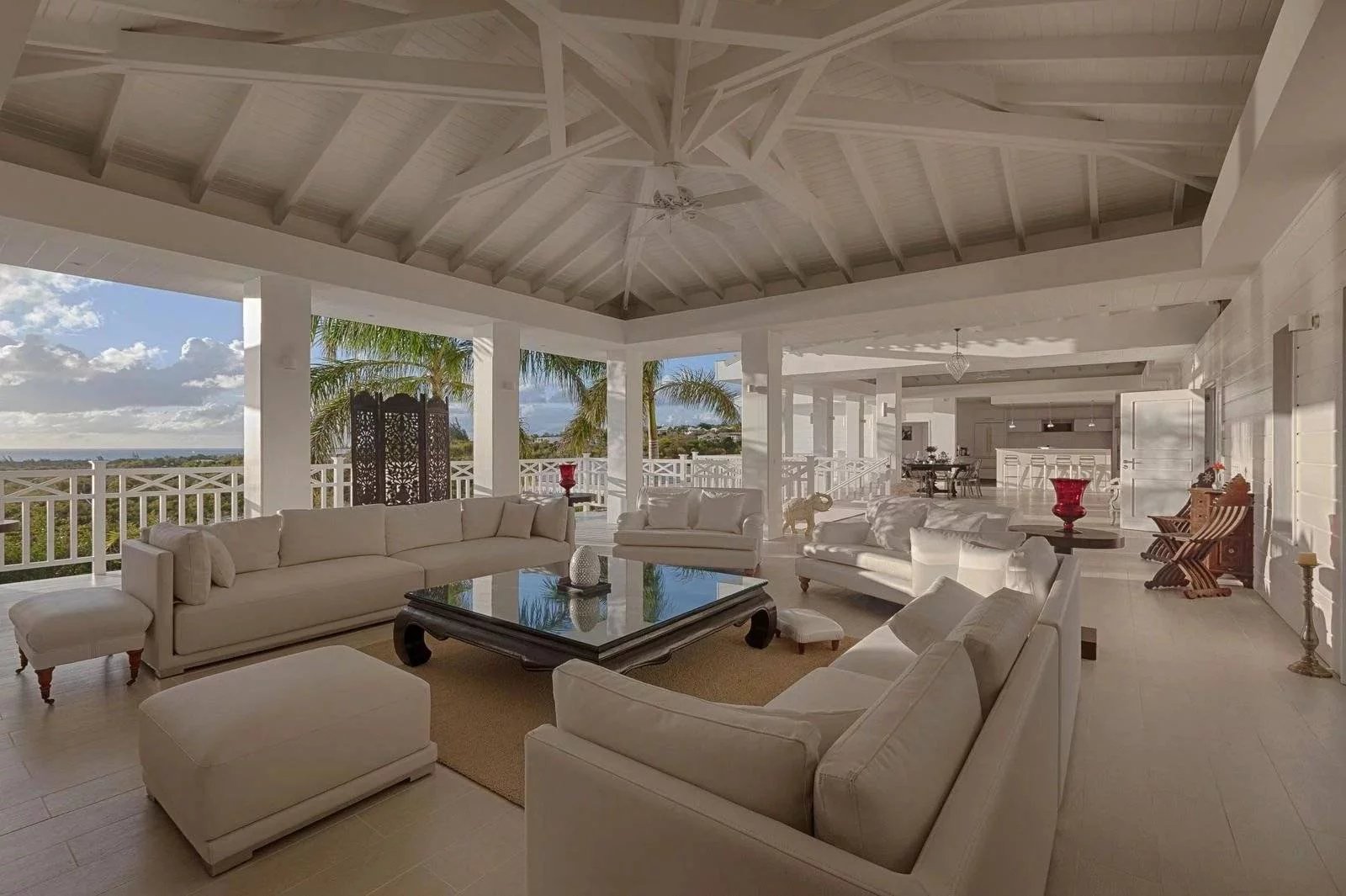 cb610b0429f3f6762bcb50c8e890766f_e0f4fe5a31_1600-original Wide open, white coastal living room with beige sofas and a glass coffee table, balcony view of palm trees and ocean.