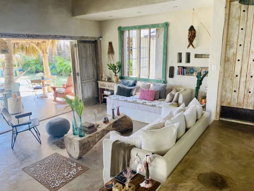 Bright bohemian living room with a white sectional, colorful pillows, and a green-framed mirror by large open doors to a sunny outdoor area