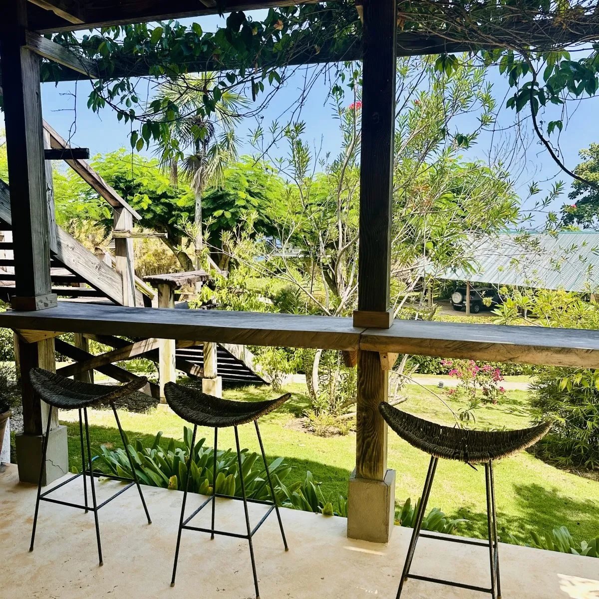 Wooden outdoor balcony with three bar-height wicker chairs facing a garden view.