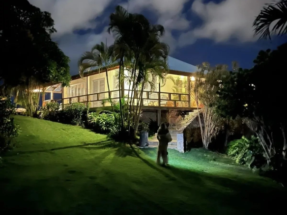 Night view of a yellow house with a wooden deck palm trees and a grassy lawn Propriétés clovis