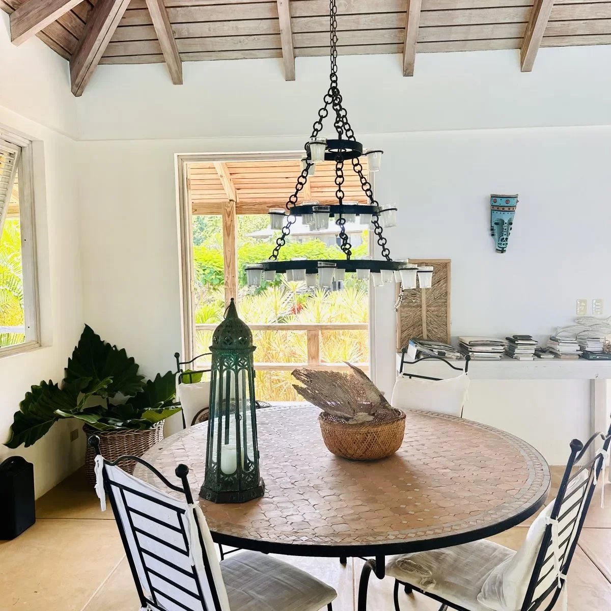 Round dining table with a mosaic tile top, black metal chairs, and a decorative teal lantern centerpiece in a bright, airy room.