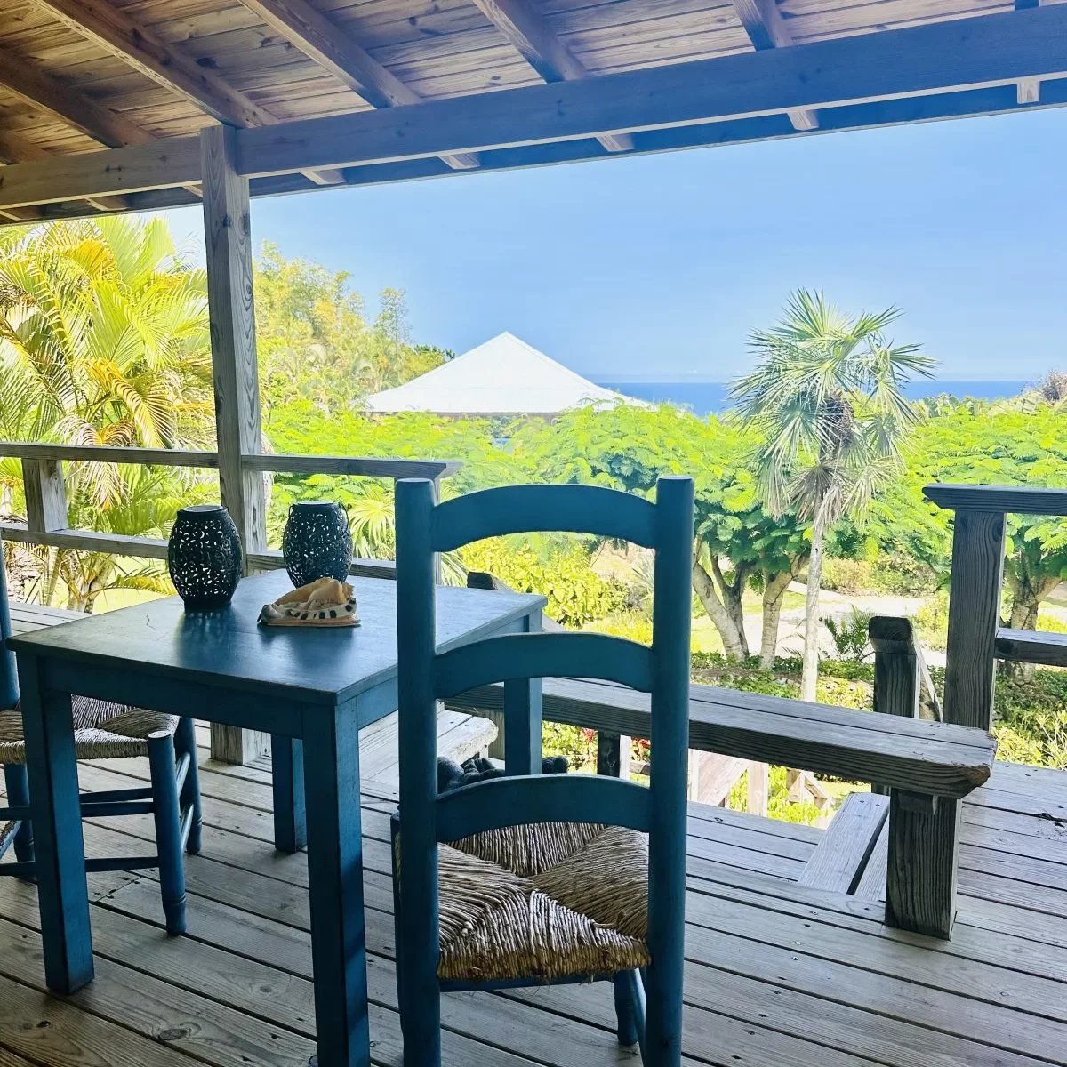 Blue wooden table and chairs on a seaside balcony with palm trees and a blue ocean in the background