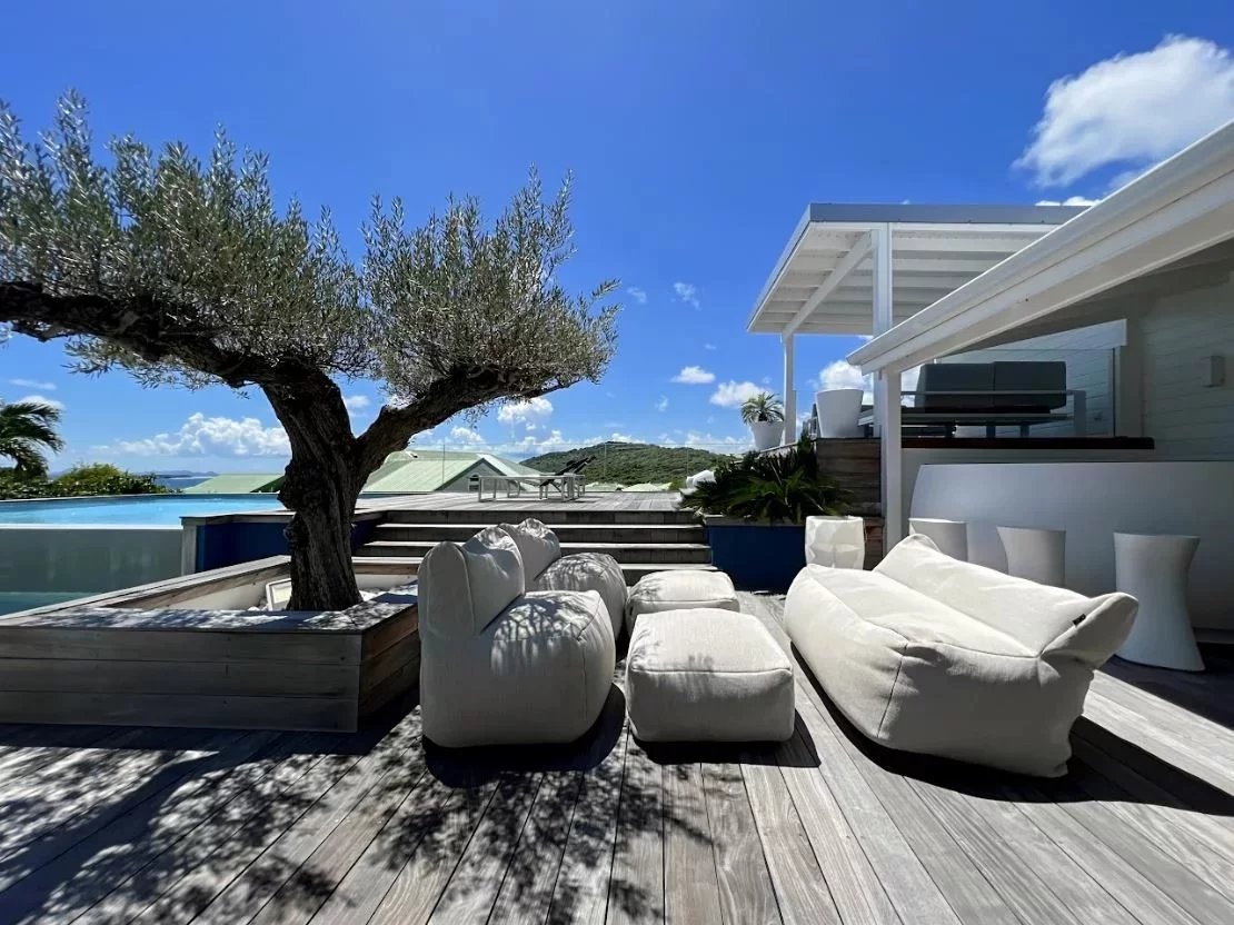 Outdoor resort deck with oversized white beanbags, a tree planter, and a pool overlooking the ocean