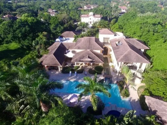 Aerial view of a large villa with brown tiled roofs and a rectangular blue pool surrounded by palm trees Propriétés clovis
