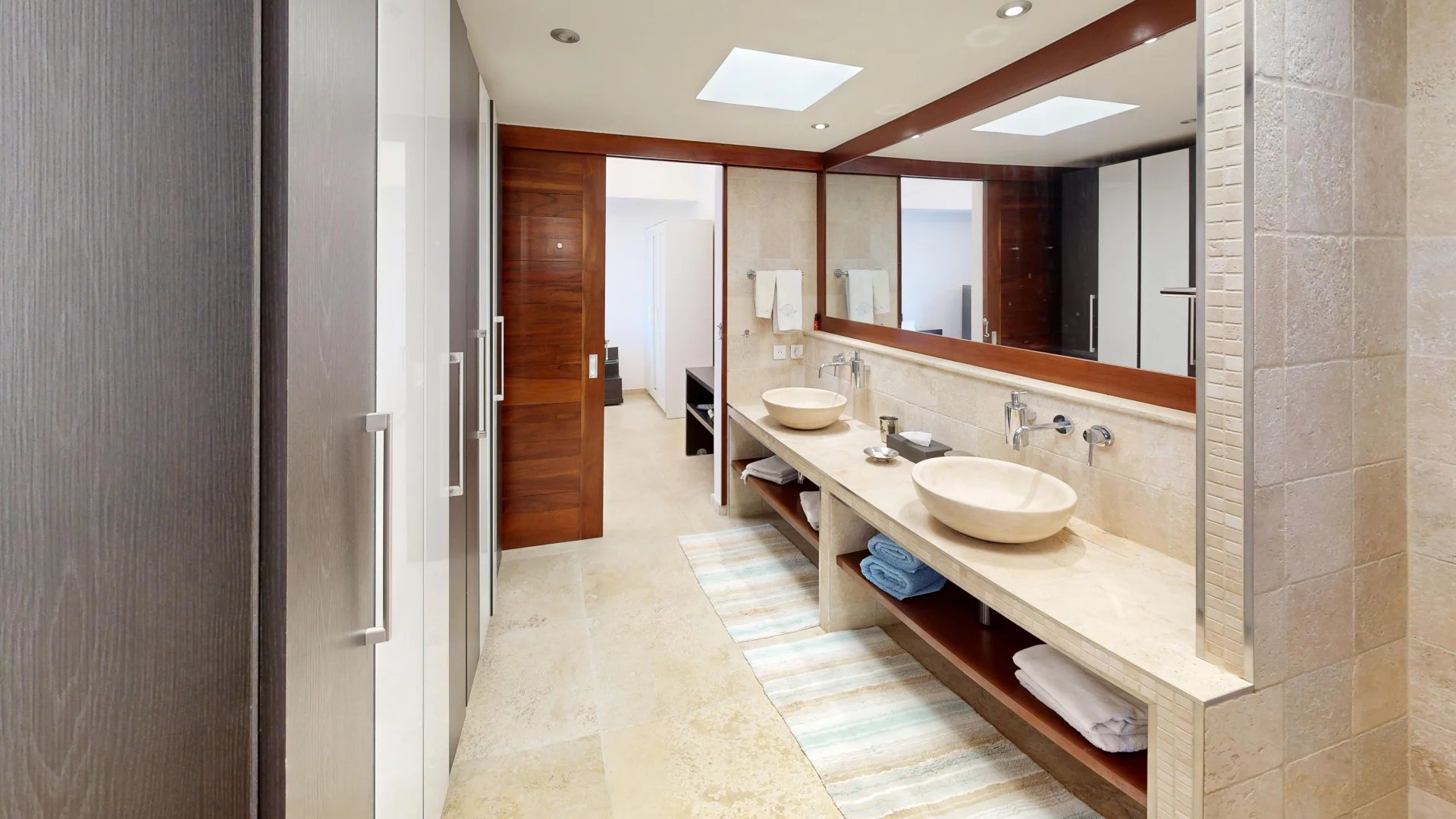Modern hotel-style bathroom with twin vessel sinks, long marble counter, and a large mirror framed in wood