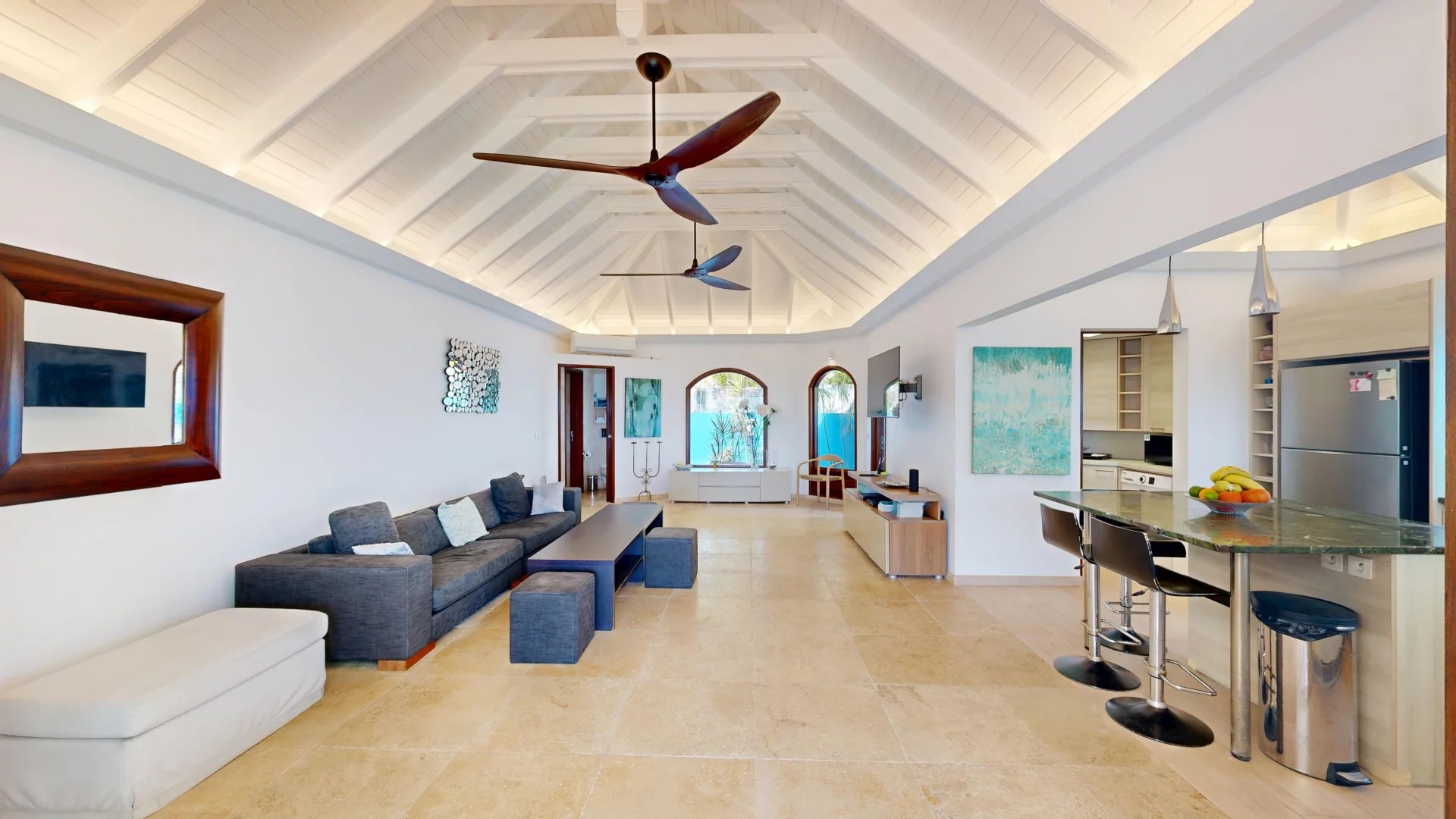 Bright open-plan living room with vaulted white ceiling, gray sectional sofa, and a marble-topped kitchen island with stools nearby.