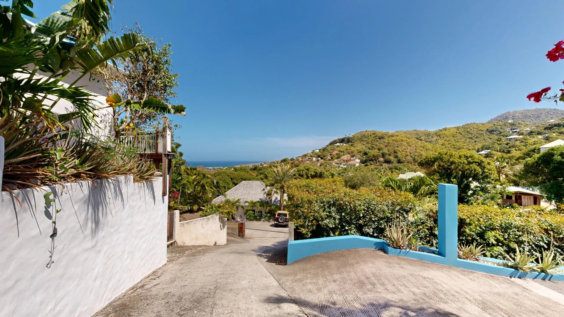 Hilltop coastal village with blue sky, green foliage, and a concrete driveway leading toward the sea.