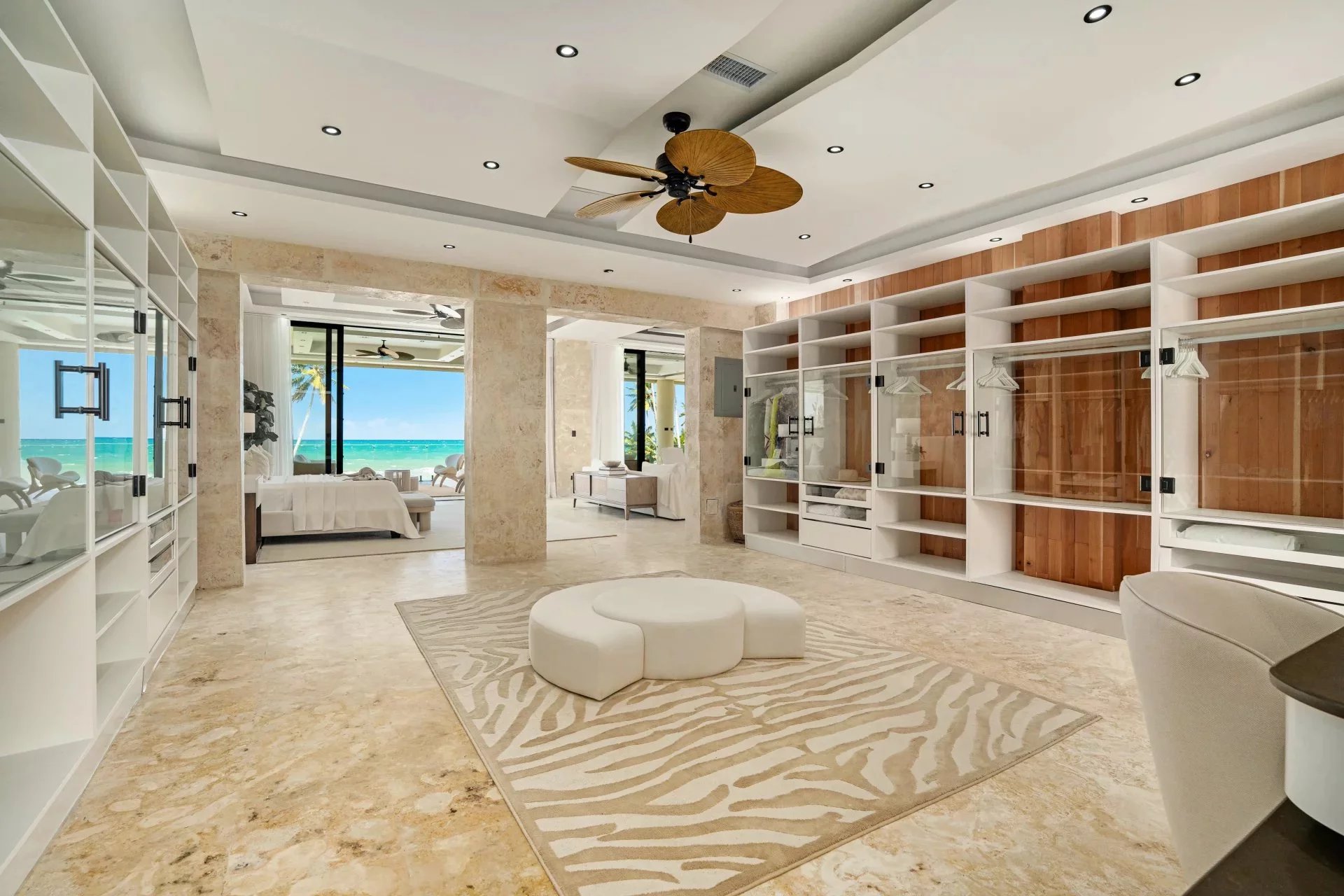 Luxurious walk-in closet with glass cabinets, white shelves, and a beach view through open doors to the sea far beyond.