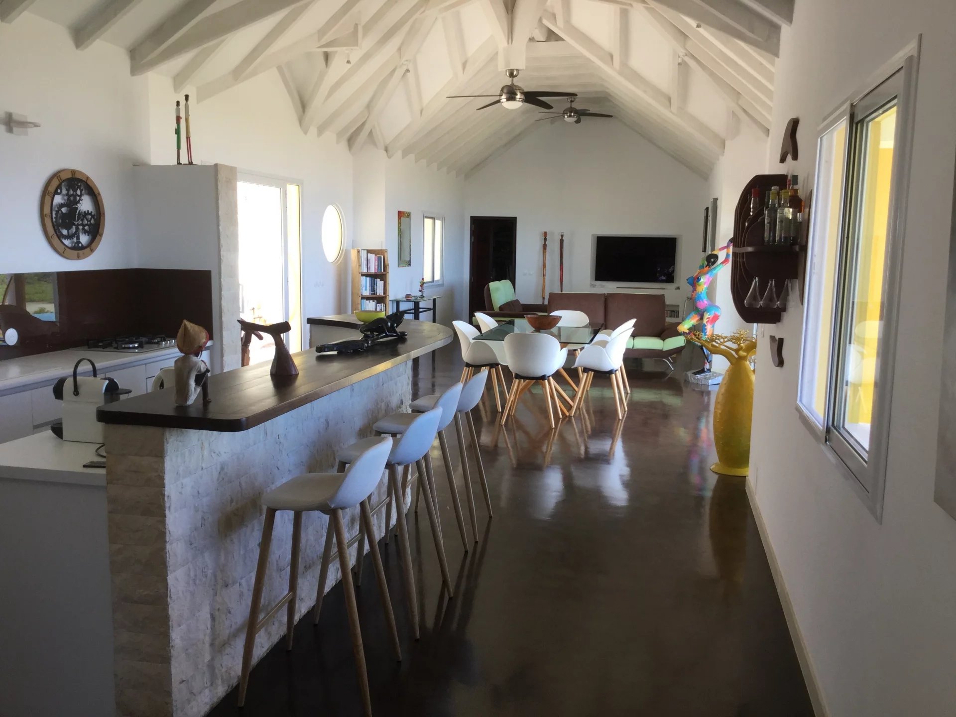 Open-concept kitchen and living area with a long stone bar and white bar stools.