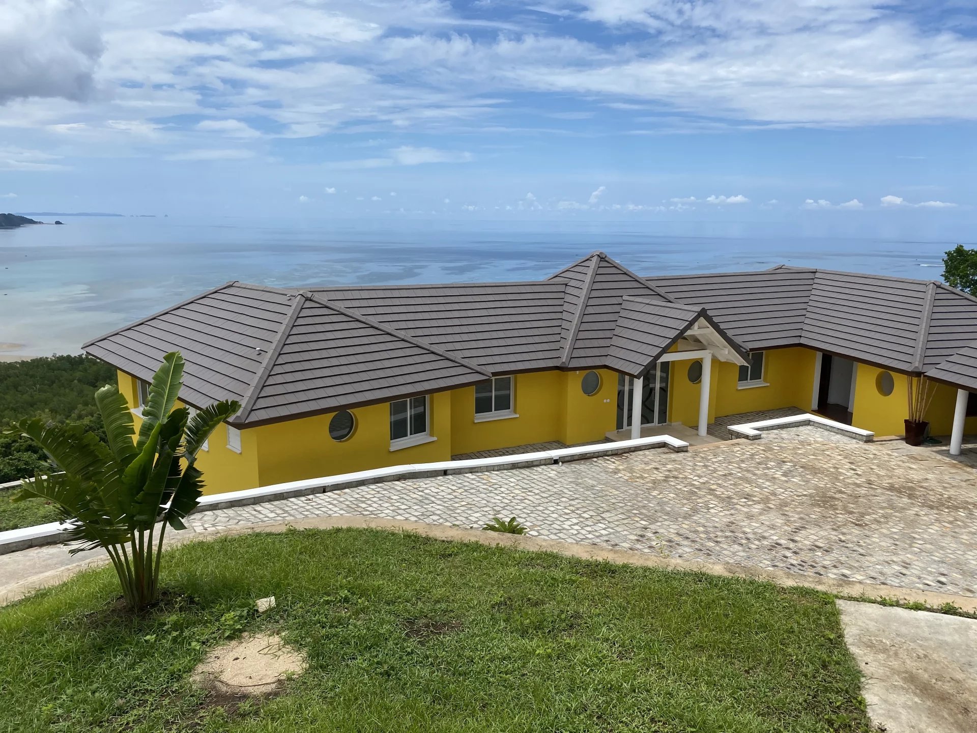 Yellow villa with gray tiled roof overlooking calm ocean and distant horizon.