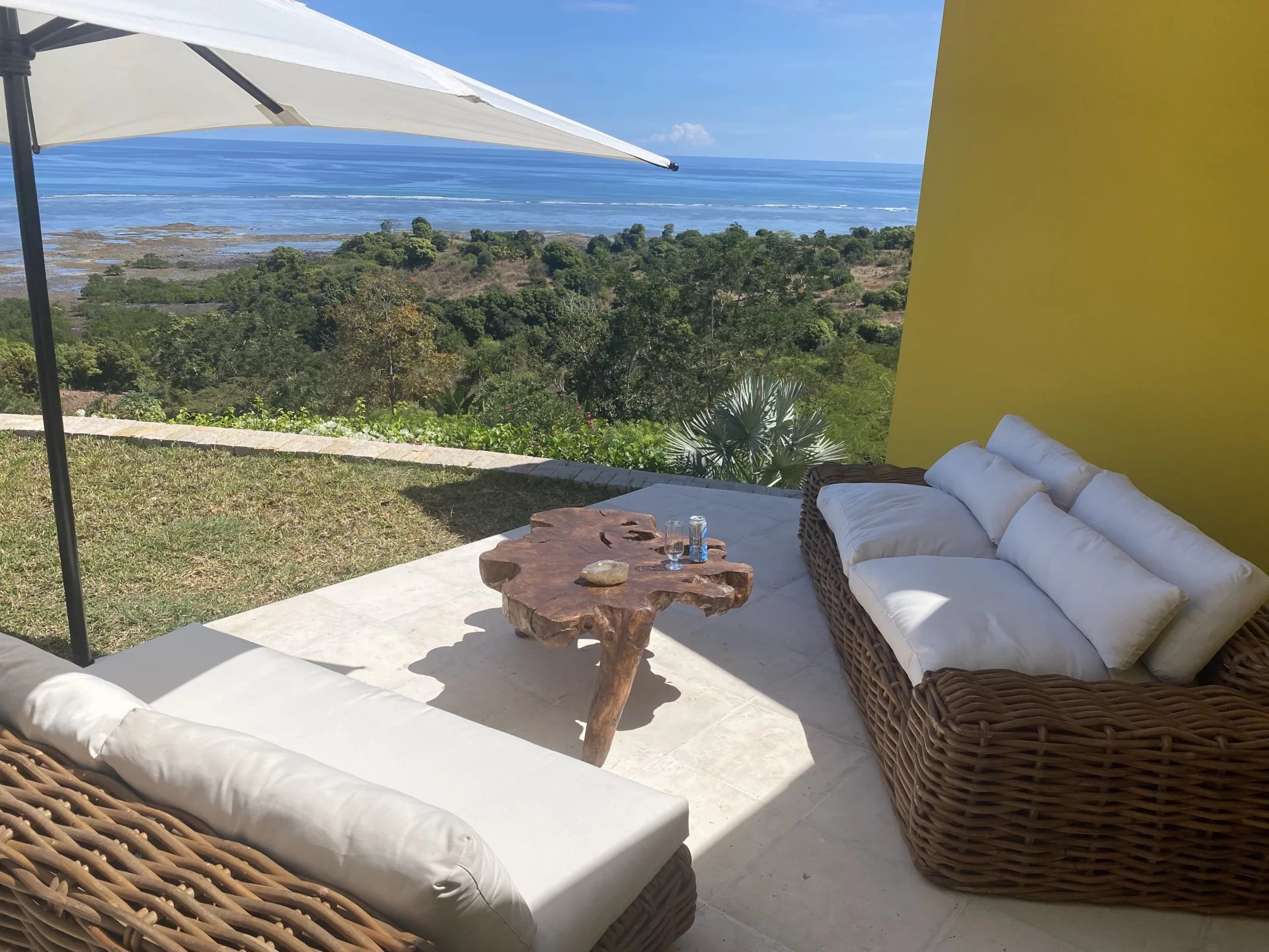 Outdoor seating area on a terrace with wicker sofas, white cushions, a natural wood coffee table, and an ocean view.