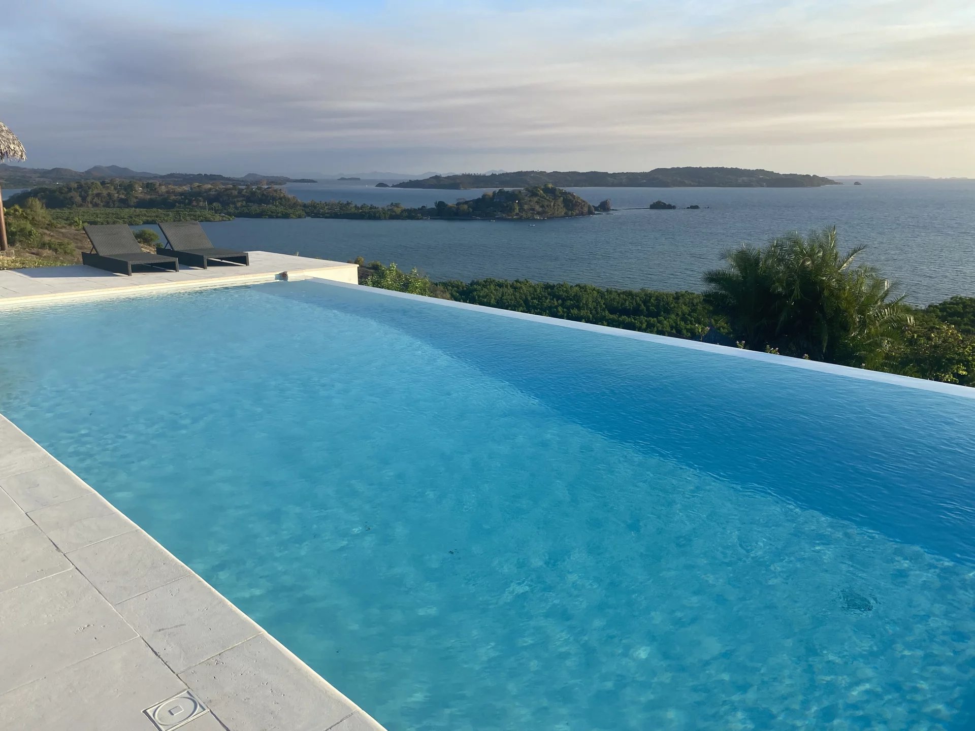 Infinity pool with a sea view: blue water, deck of lounge chairs, and distant islands.